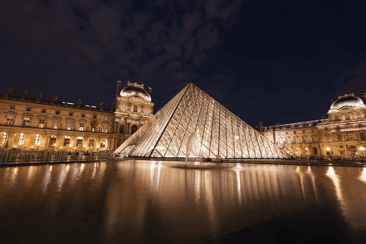 The glass pyramid of the Louvre lit up at night, reflected in the water